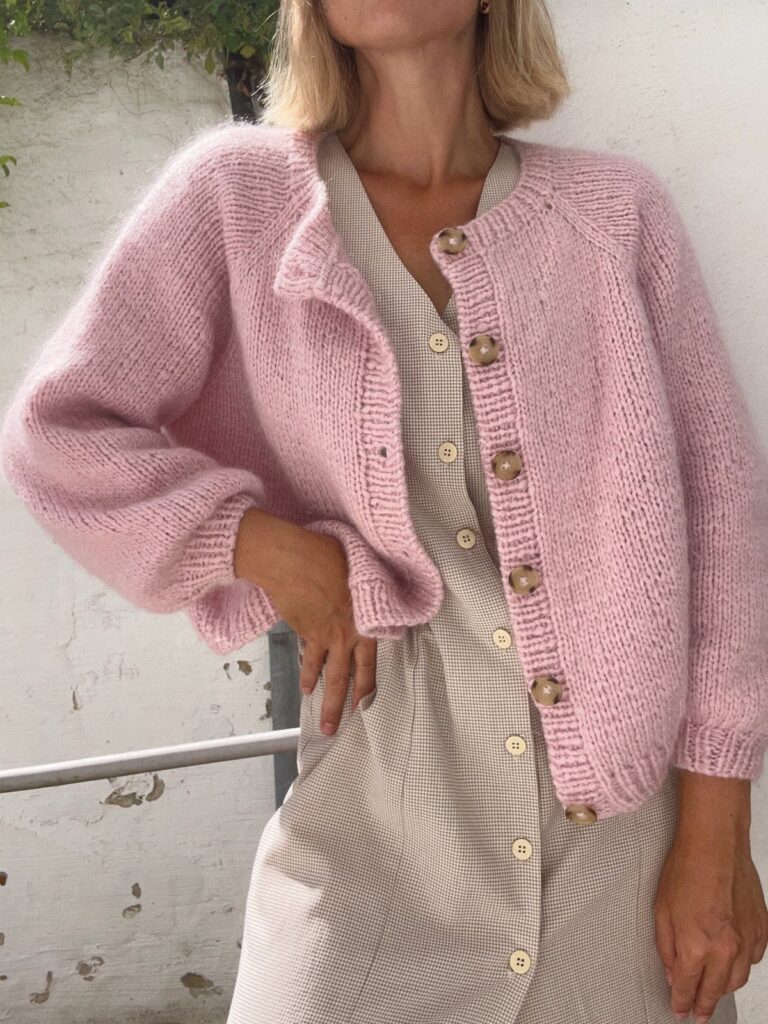 Woman wearing a light pink knit cardigan over a beige button-down midi dress.
