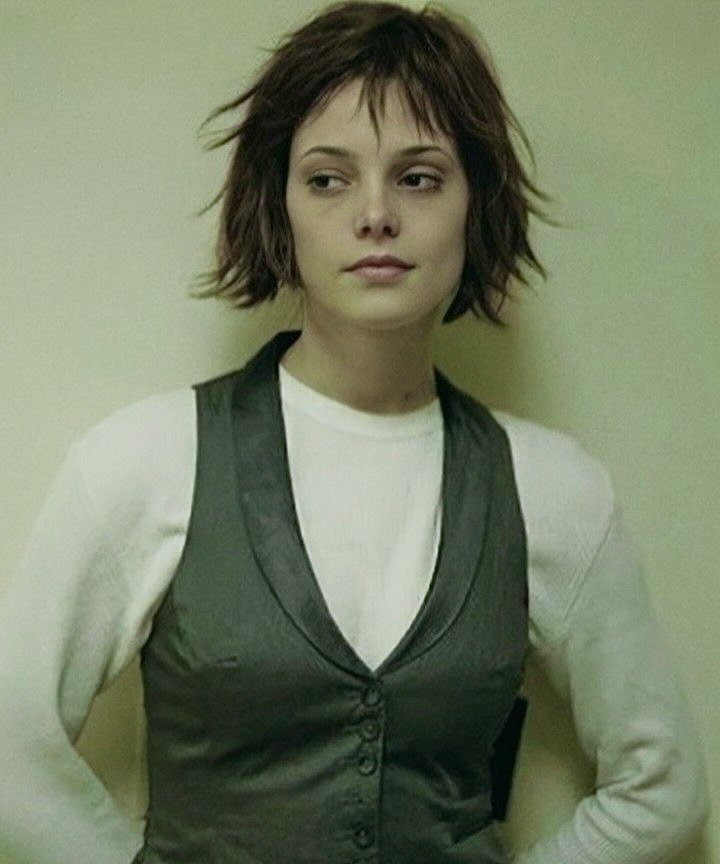 Woman with short brown hair wearing a white shirt and grey vest.