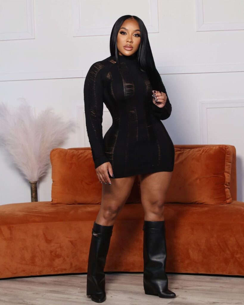 Black woman wearing a short black long-sleeved dress and tall black leather boots.