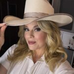 Woman wearing a wide-brimmed beige straw hat and a white button-down shirt.