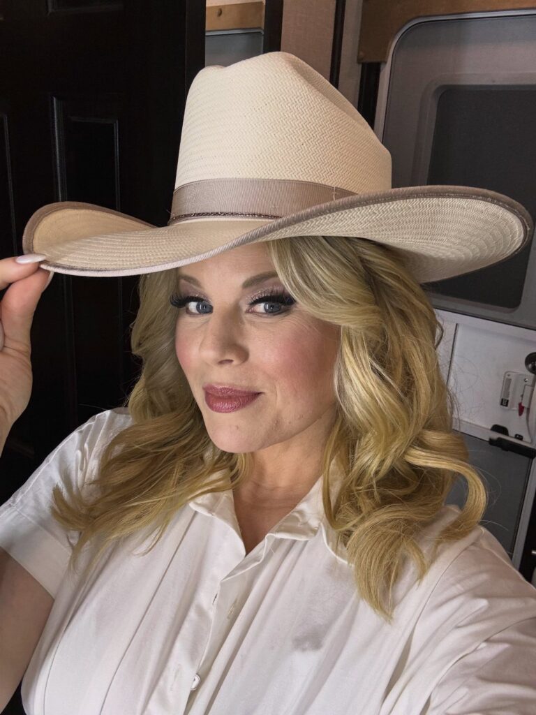 Woman wearing a wide-brimmed beige straw hat and a white button-down shirt.