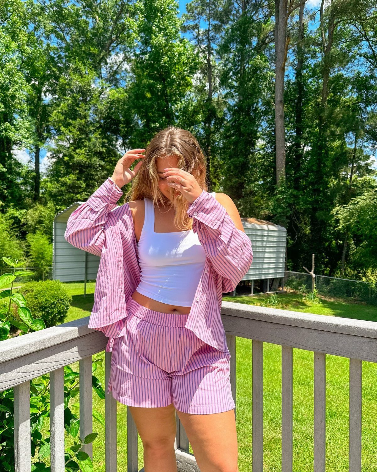 Woman wearing a pink striped summer set with a white crop top on a deck.