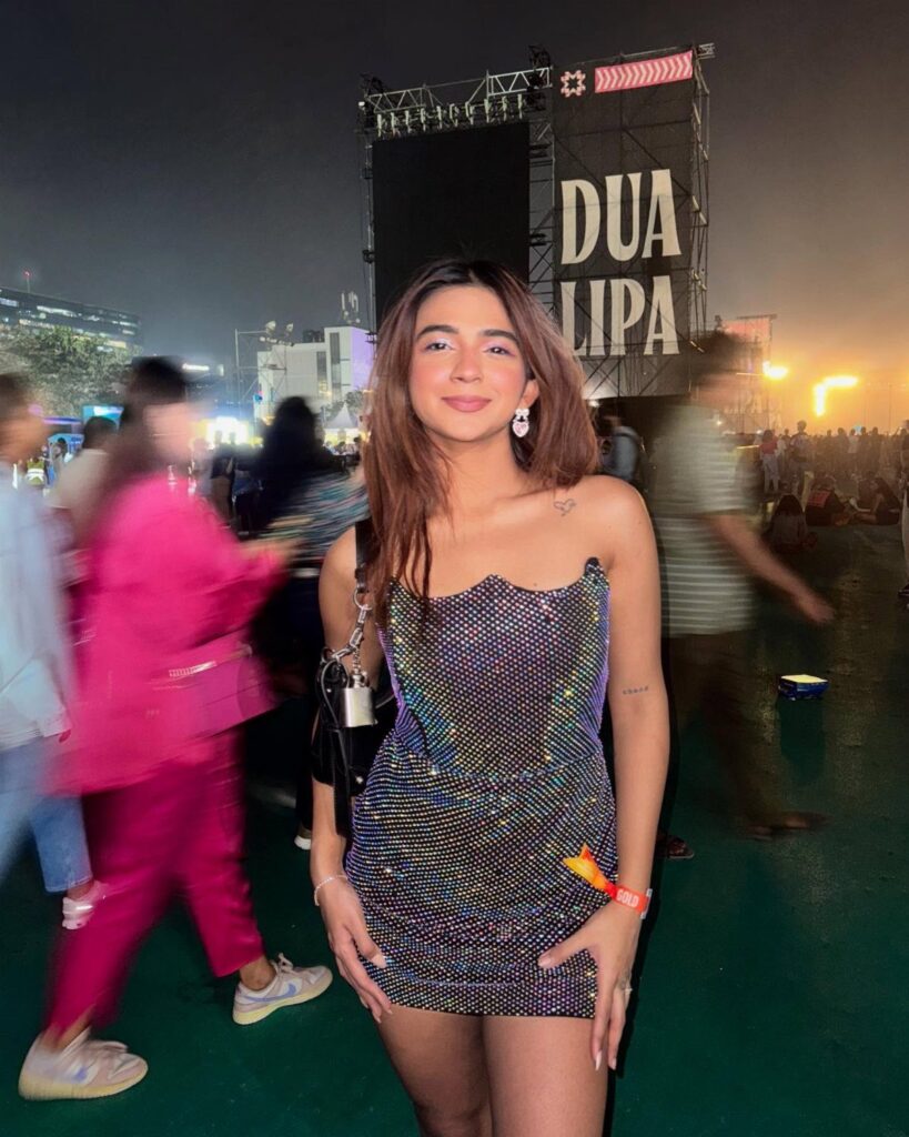 Woman wearing a sparkly purple mini dress at a Dua Lipa concert venue.