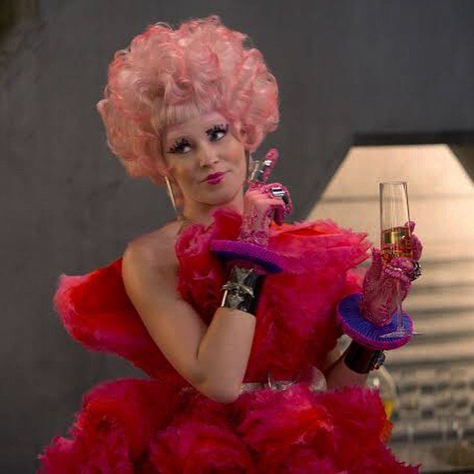 Woman in a voluminous pink ruffled dress and pink curly wig holding champagne.