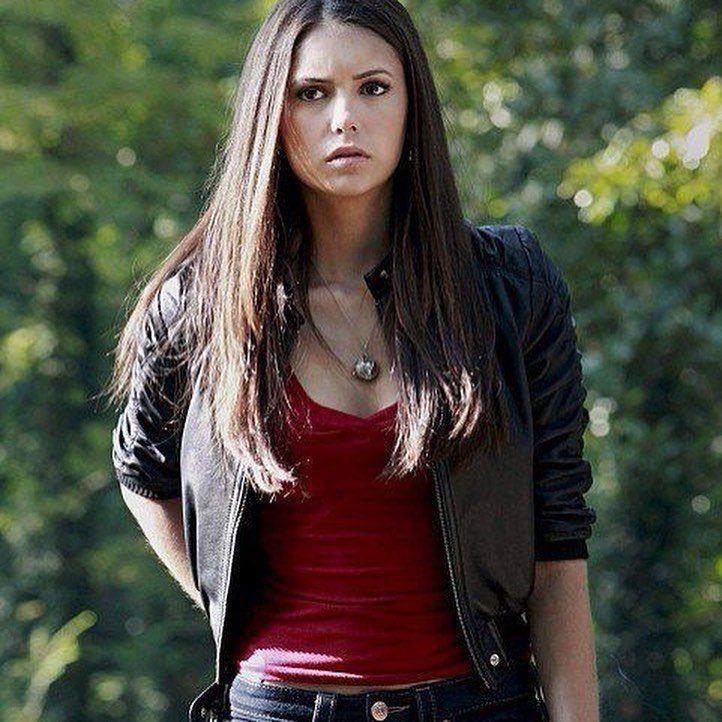 Woman wearing a red shirt and black leather jacket in a forest setting.
