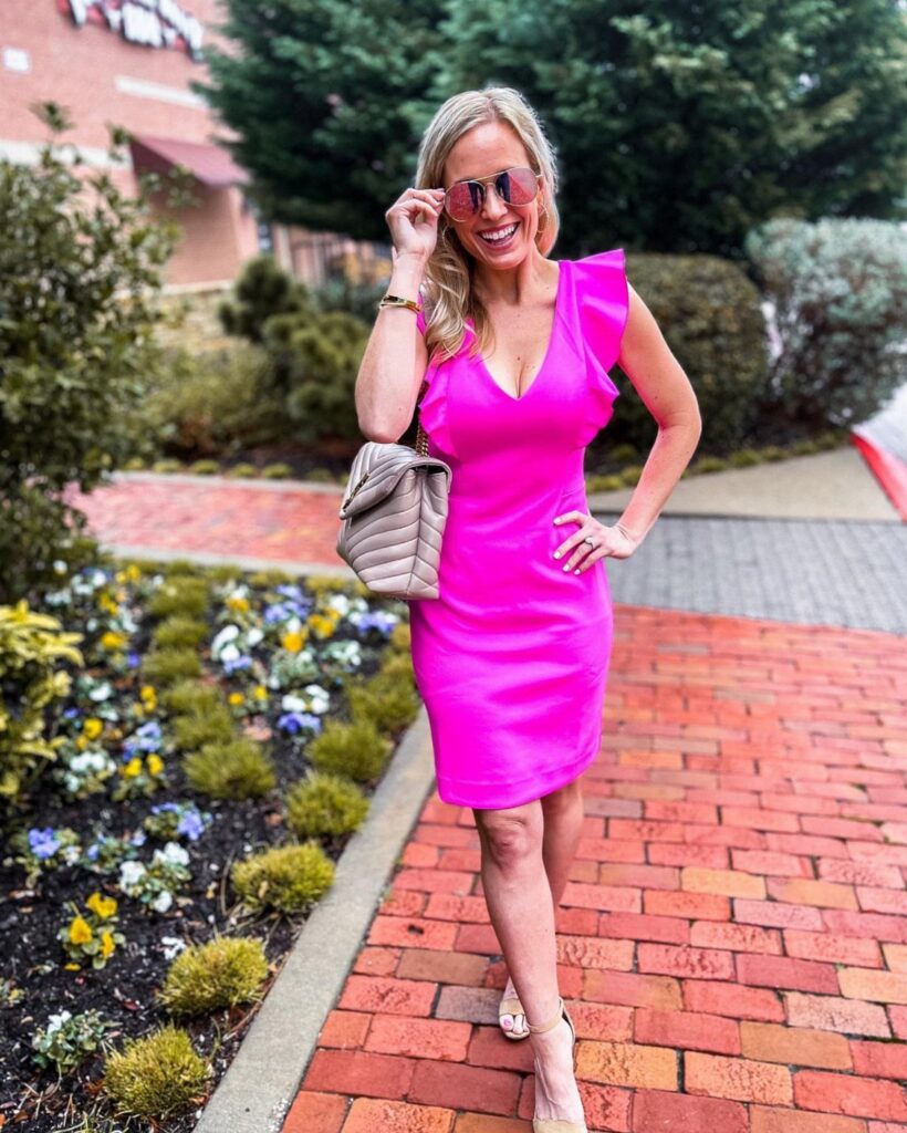 Woman in a bright pink dress and sunglasses posing on a brick walkway.