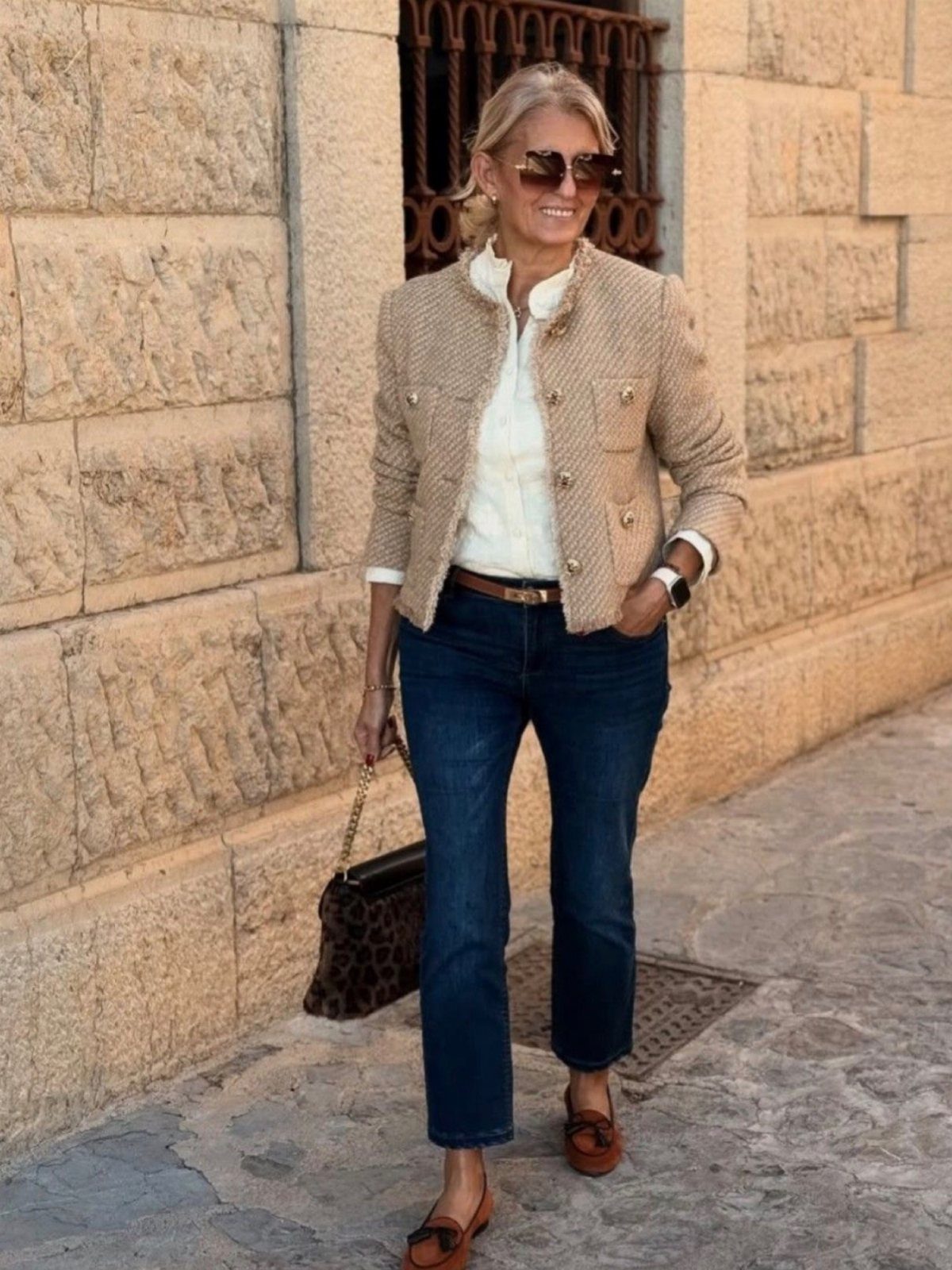 Woman wearing dark blue denim jeans, a beige jacket, and leopard print handbag.