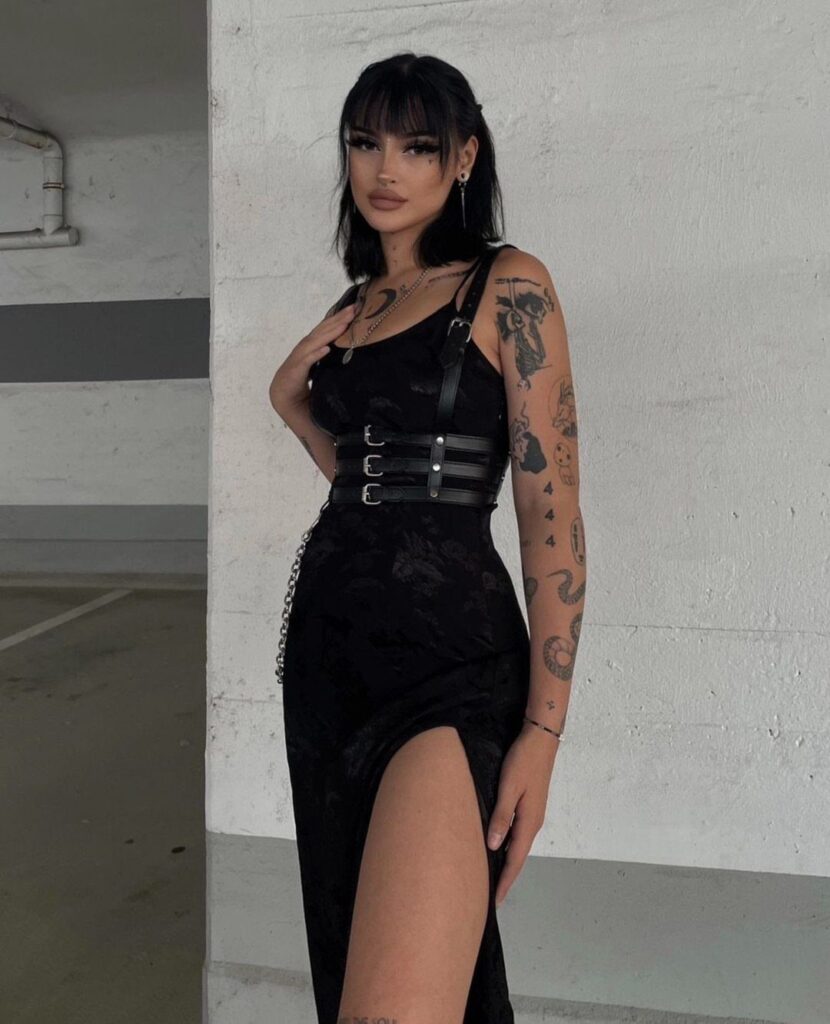 Woman in a black gothic dress with a buckled belt and high slit.