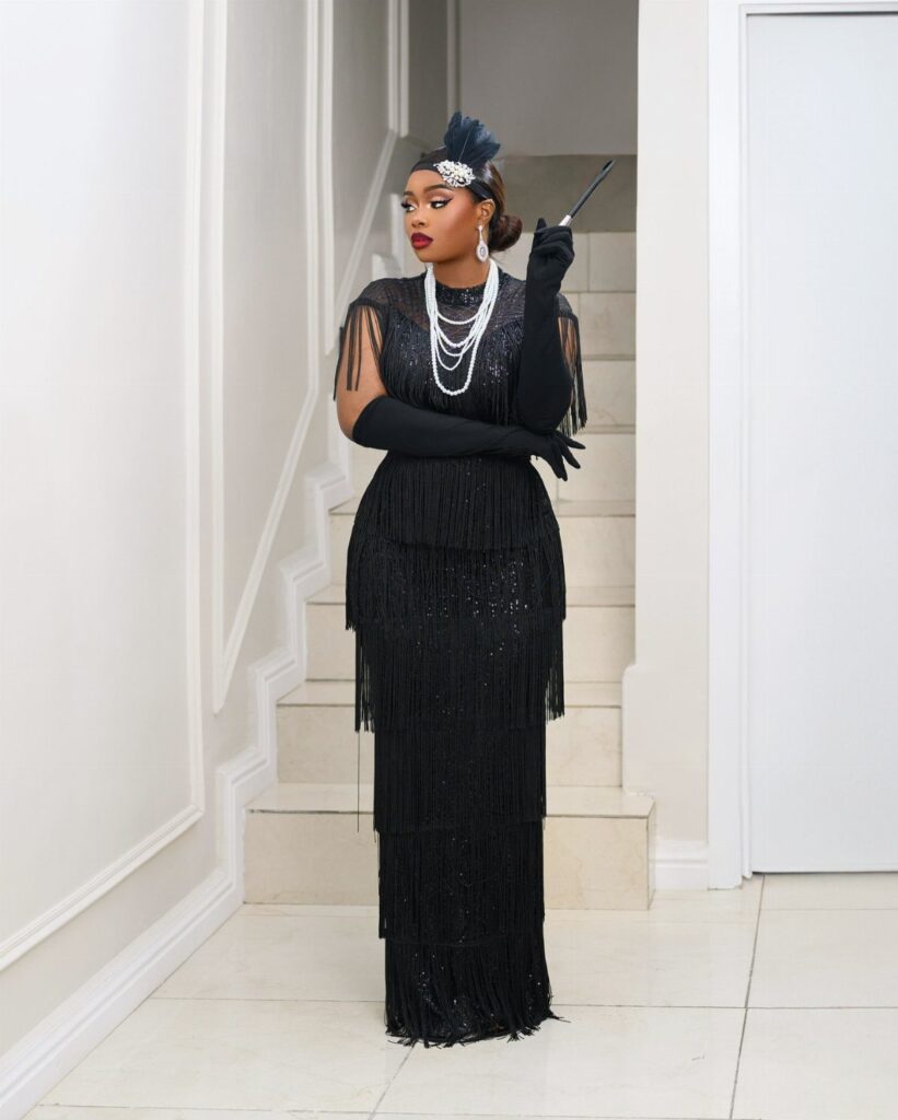 Woman in a black sequined flapper dress with pearls and a feathered headpiece.