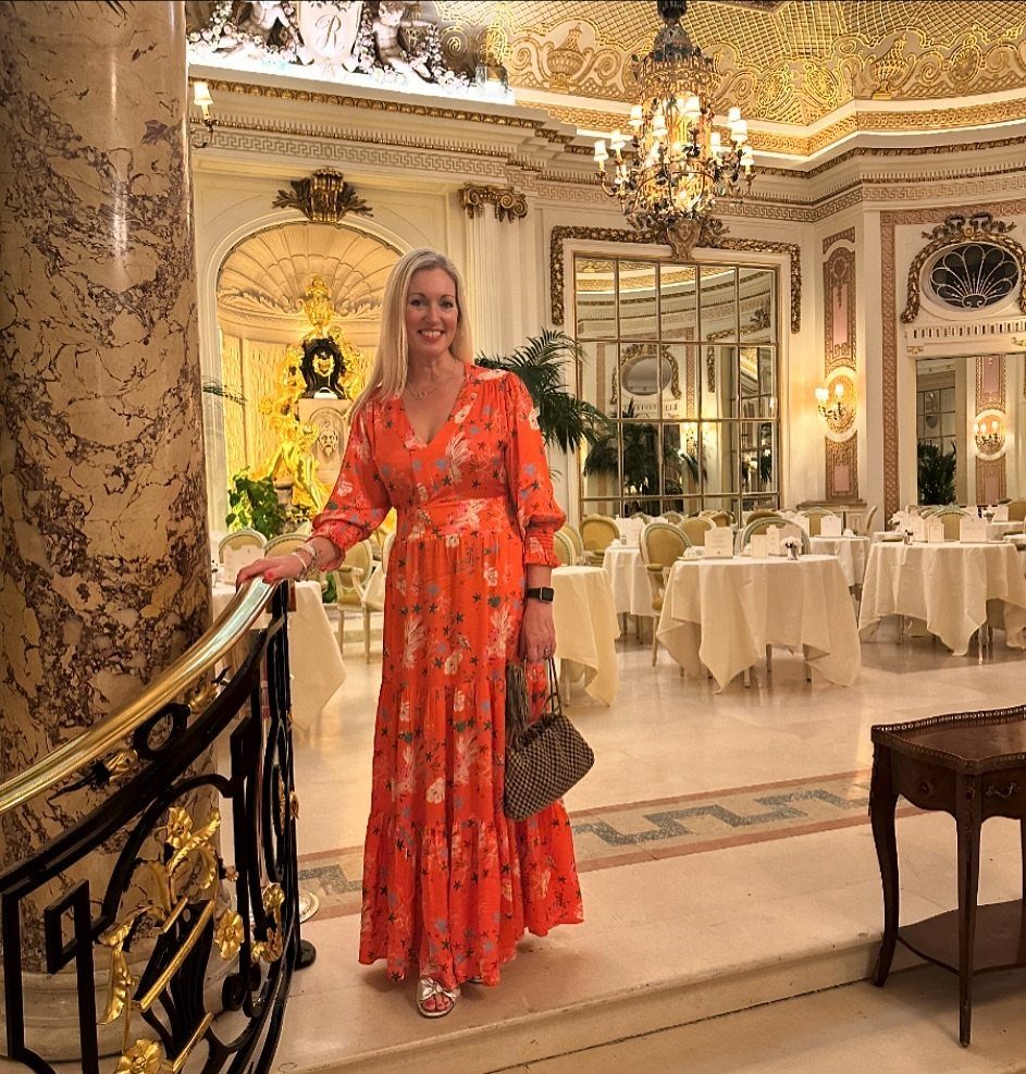 Woman in orange floral maxi dress posing in a luxury hotel dining room