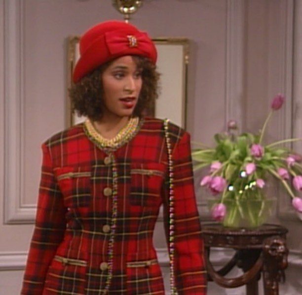 Woman in red plaid blazer and matching hat with gold jewelry and pink tulips.