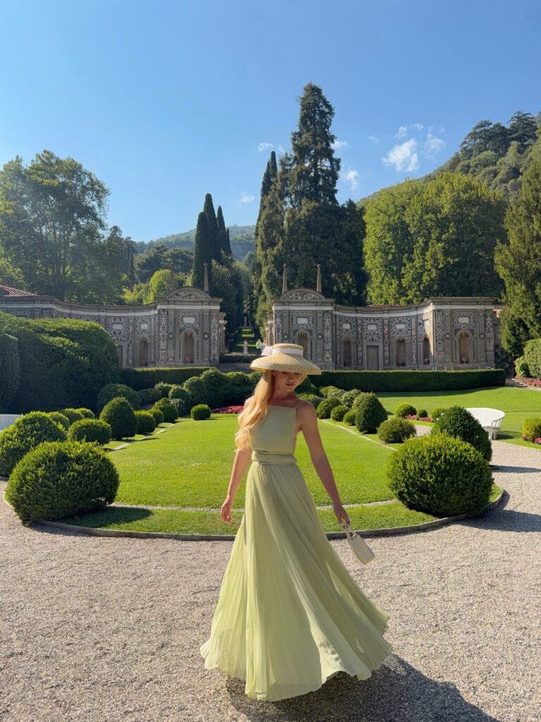Woman in a long pastel green dress and straw hat in a formal garden.