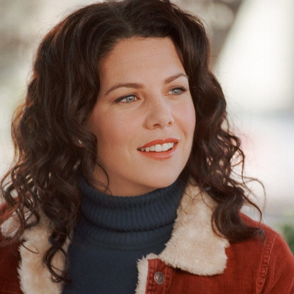 Woman with curly brown hair wearing a dark blue turtleneck and rust corduroy jacket.