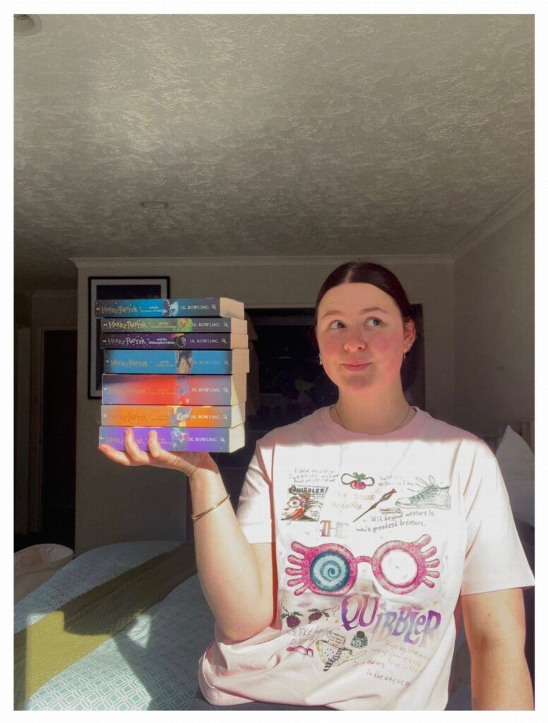 Woman wearing a pink t-shirt with Luna Lovegood's spectresicles and holding Harry Potter books.
