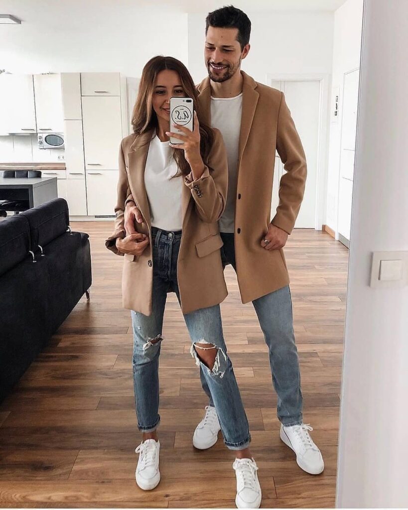 Couple wearing matching tan coats, white shirts, blue jeans, and white sneakers.