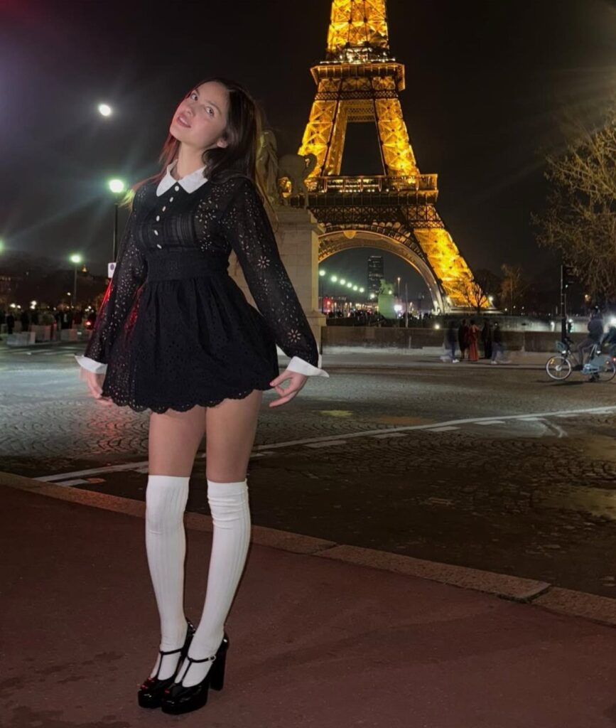 Young woman in a black mini dress and white knee-high socks before the Eiffel Tower.