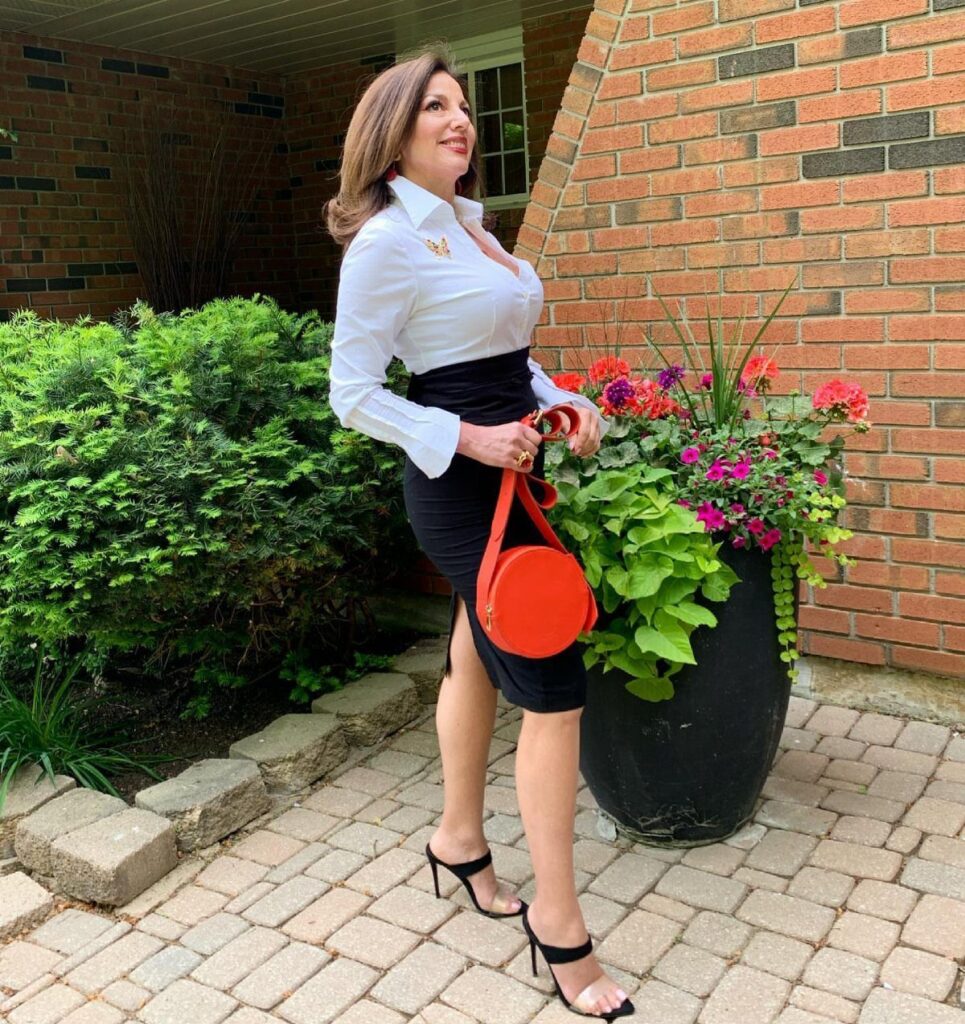 Woman wearing a white shirt and black pencil skirt with a red handbag.