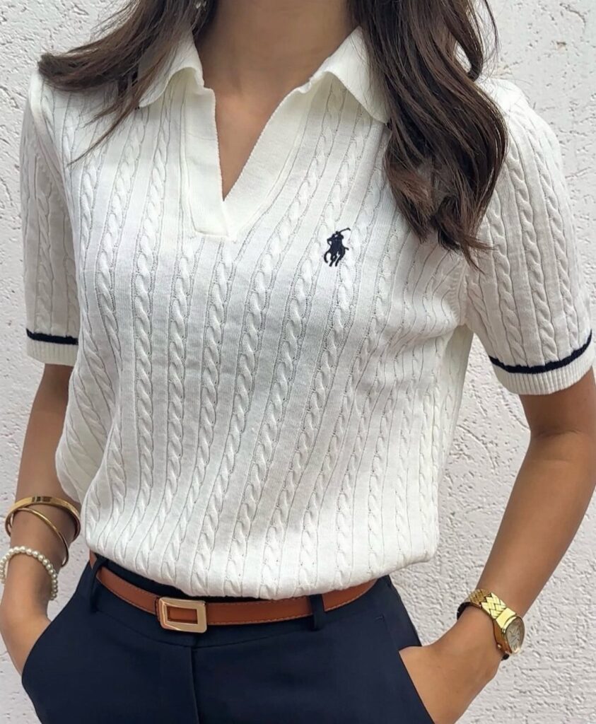 White cable-knit polo shirt tucked into navy trousers with a brown leather belt.