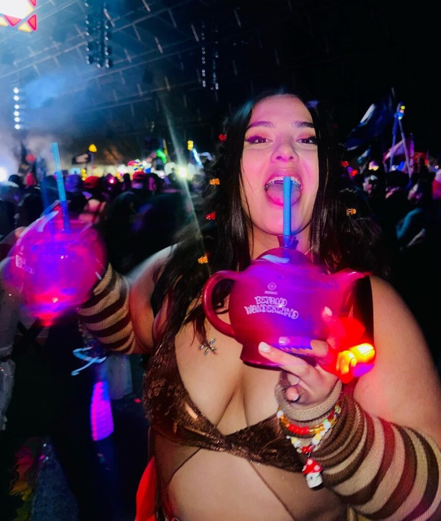 Plus size woman in gold metallic rave outfit holding a pink teapot drink