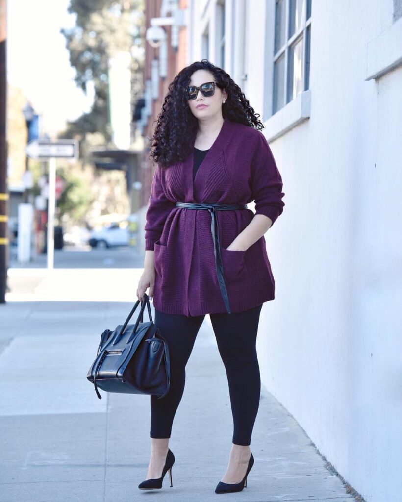 Woman wearing a chunky purple knit cardigan with a belt and black leggings.