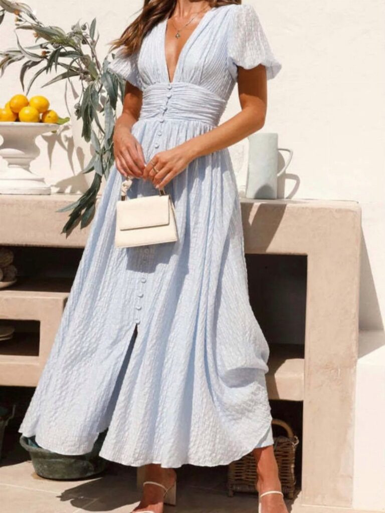 Woman in a light blue V-neck maxi dress holding a small white handbag.
