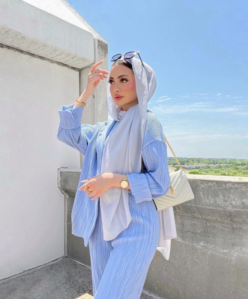 Woman in a white hijab and blue striped summer suit posing on a balcony.