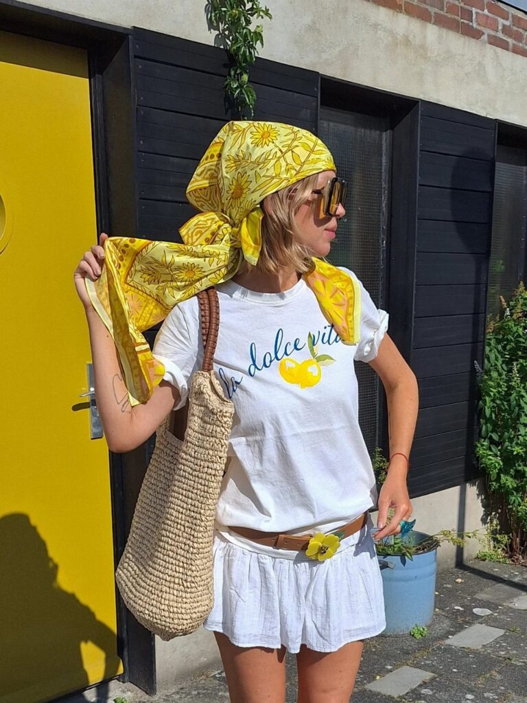 Woman wearing a yellow headscarf and sunglasses with a white summer outfit.