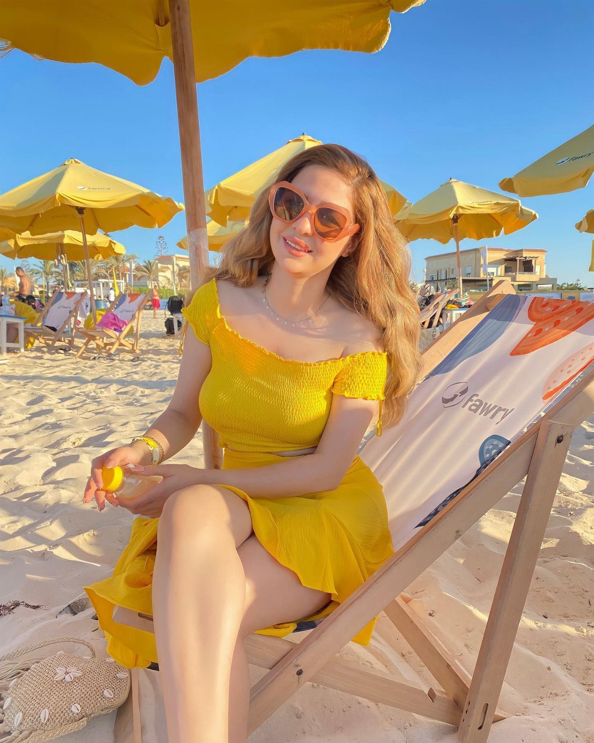 Woman in a yellow off-the-shoulder dress and sunglasses relaxing on a beach chair.