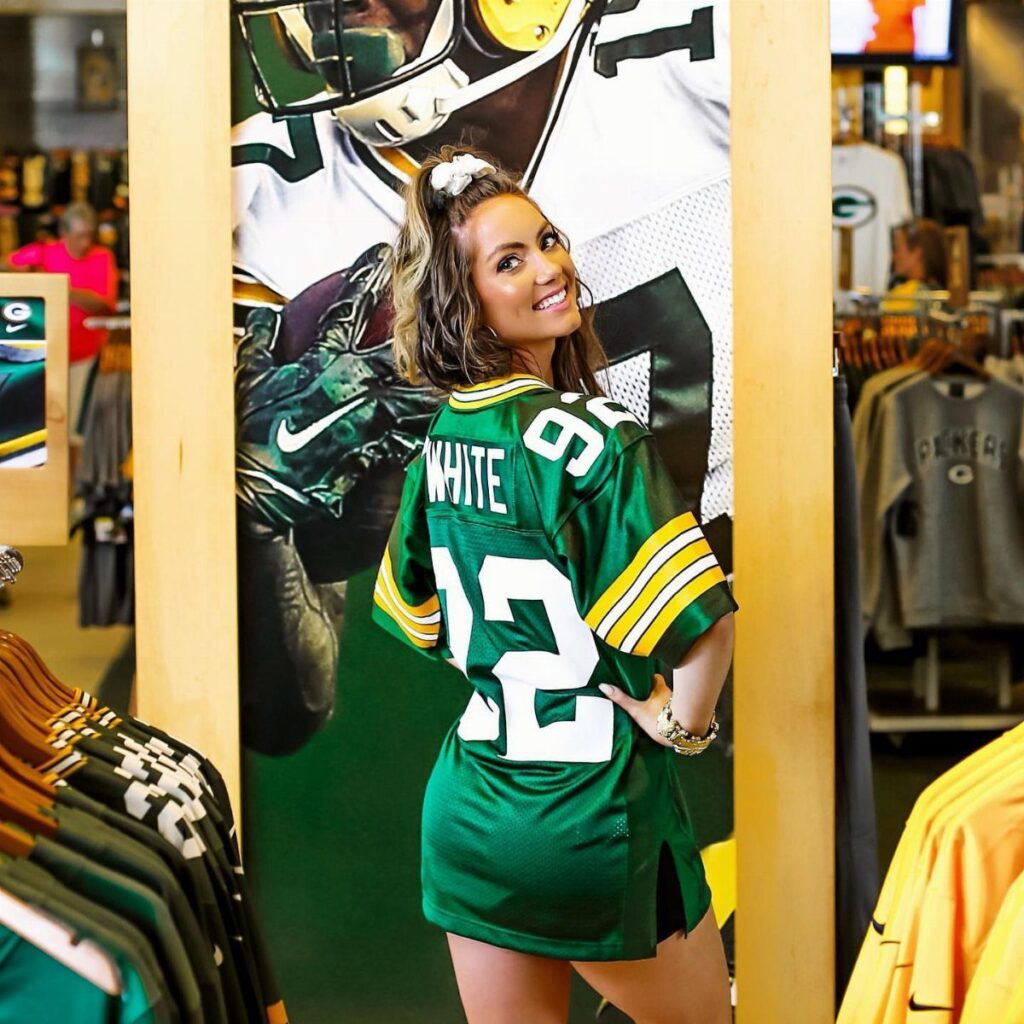 Woman wearing an oversized green football jersey as a dress in a sports store.