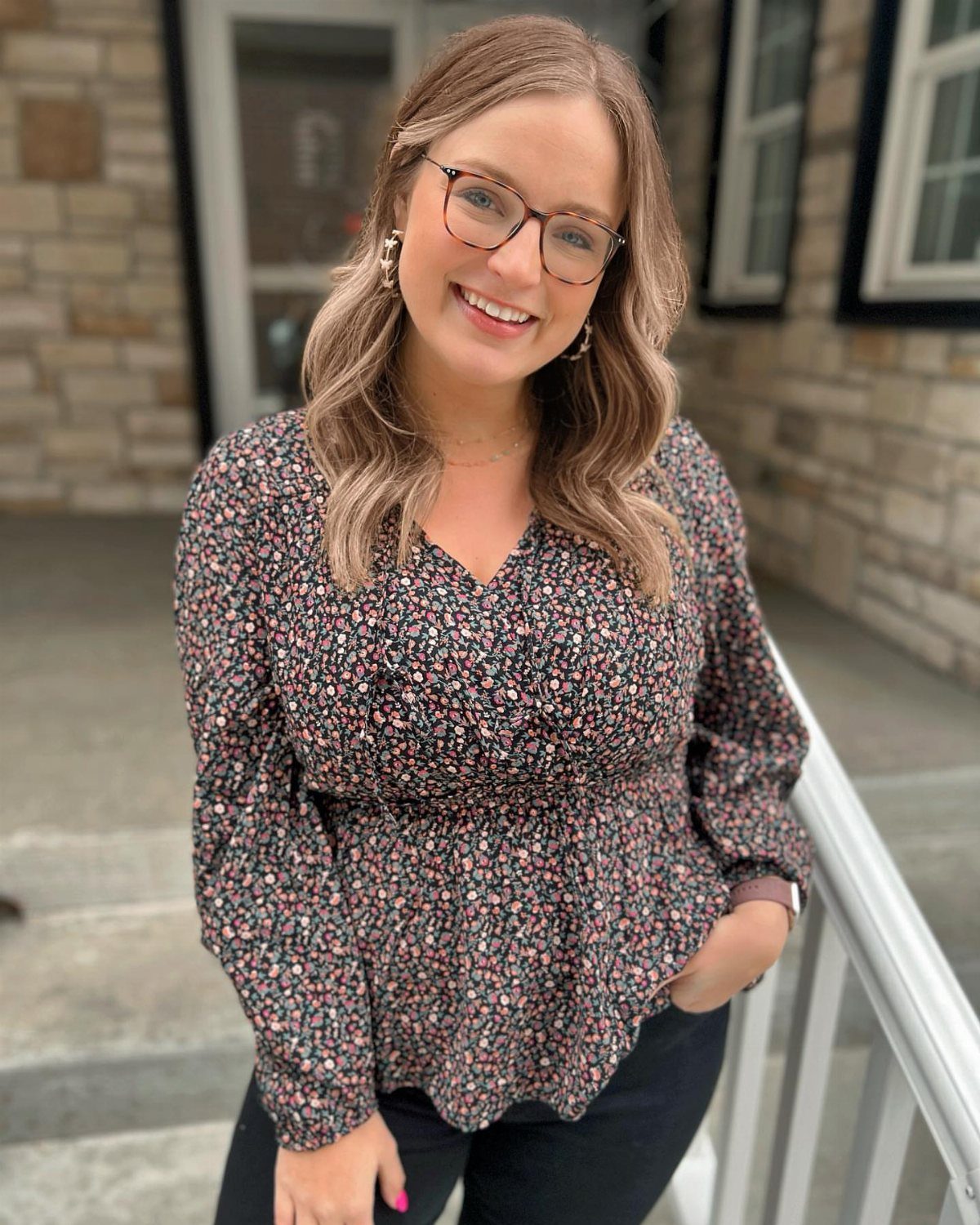 Woman wearing a floral print peplum top and black pants standing outdoors.