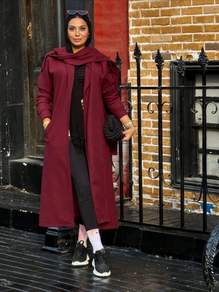 Woman wearing a long burgundy scarf coat with black trousers and sneakers.